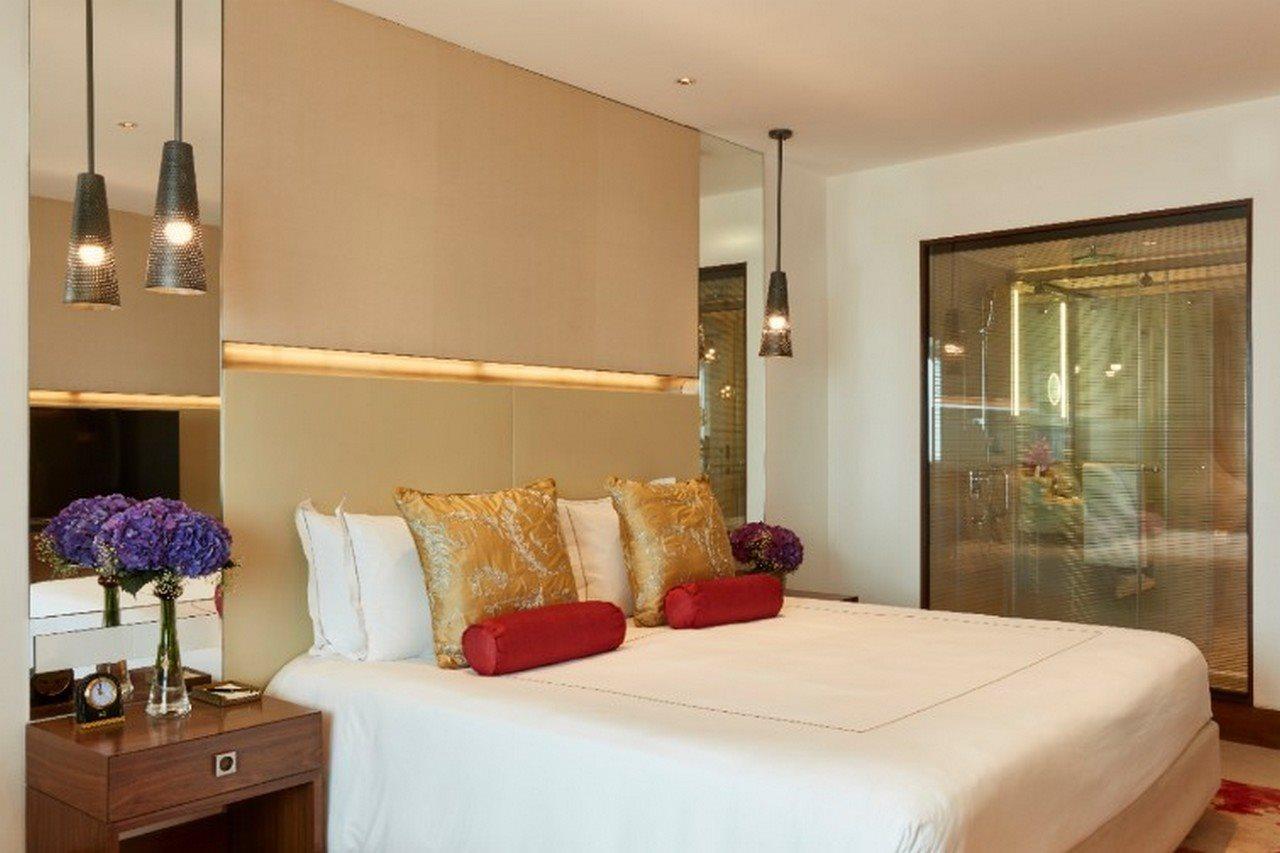 The Taj Mahal Tower, Mumbai Hotel Buitenkant foto The photo shows a modern bedroom with a stylish design. It features a large bed with white linens and decorative pillows in gold and red. The walls are neutral, and there are pendant lights hanging above the bed. To the side, there is a wooden nights