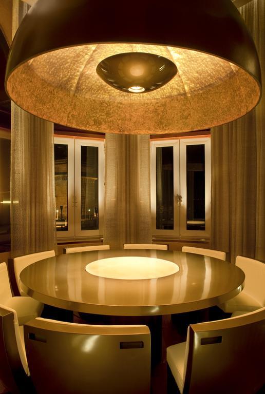 The Taj Mahal Tower, Mumbai Hotel Buitenkant foto The photo shows a modern dining room with a round table at the center. The table has a glossy surface and features a circular illuminated section in the middle. Surrounding the table are sleek, contemporary chairs. The room has large windows dressed 