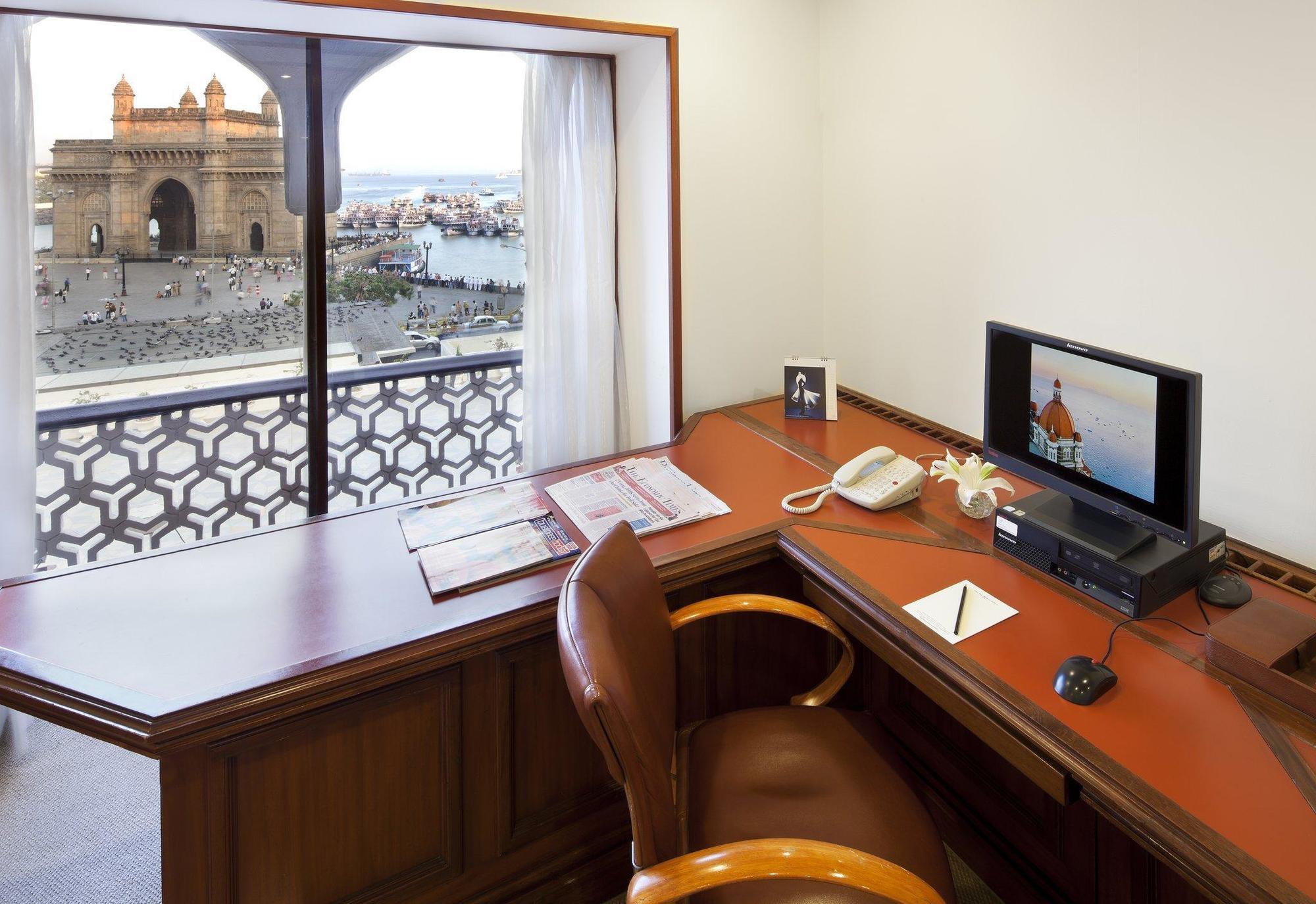 The Taj Mahal Tower, Mumbai Hotel Buitenkant foto The photo shows a workspace with a wooden desk and an ergonomic chair. On the desk, there is a computer monitor, a telephone, and some stationery items. A window provides a view of an outdoor scene, possibly featuring water and structures or building