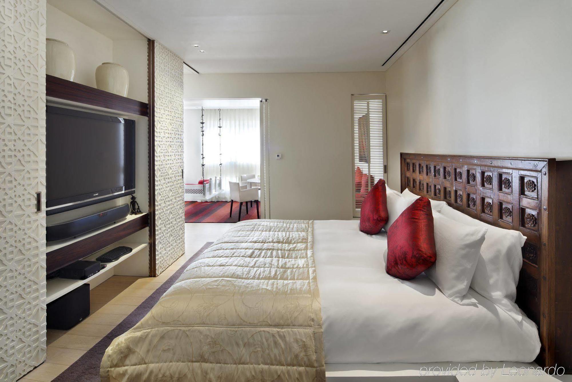 The Taj Mahal Tower, Mumbai Hotel Buitenkant foto The photo depicts a modern hotel bedroom. The room features a large bed with white bedding and decorative red pillows. A beautifully carved wooden headboard adds an elegant touch. In the background, there is a flat-screen TV mounted on the wall, alon