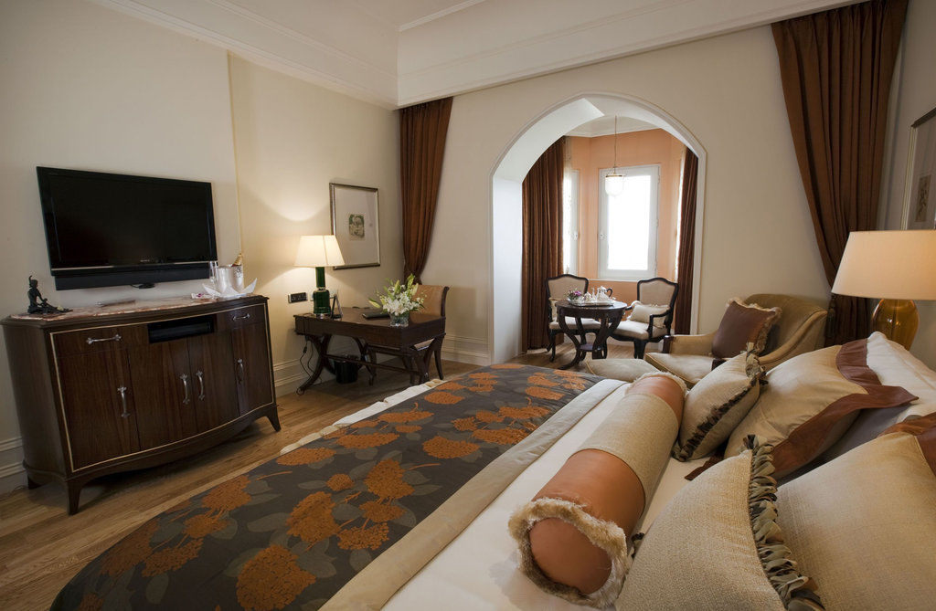 The Taj Mahal Tower, Mumbai Hotel Buitenkant foto The photo shows a beautifully arranged hotel room featuring a king-size bed with decorative pillows and a stylish bedspread. Beside the bed is a modern wooden dresser with a flat-screen TV mounted on the wall. There is a cozy seating area with two ch